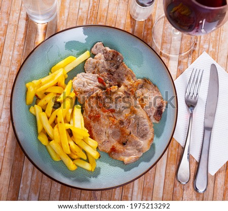 A picture of a pork chop on a plate of fried potatoes.