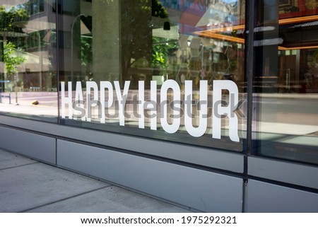 Closeup of the Happy Hour storefront sign at a modern restaurant and bar in the downtown district of a city. Happy Hour is a marketing strategy to boost sales during slower weekday shifts.