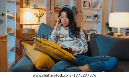 Thoughtful Asia lady holding phone feeling sad waiting for call sit at sofa in living room at house night feel lonely, Sad depressed teenager spend time alone, Social distance, Coronavirus quarantine. Royalty-Free Stock Photo #1975297376
