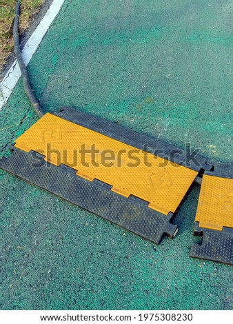 Black and yellow heavy plastic covers for people and vehicle to cross over cables laid on road. Pavement pads to protect electrical wiring on sidewalk in public park. Channel for laying the wires.
