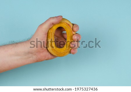 The hand is clutching a yellow rubber band on a blue background. Adult male holding a hand-held round hand trainer. Side view. Sports, active lifestyle.