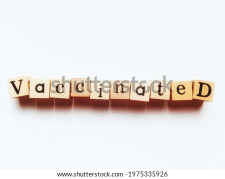 Top view photo of square wooden blocks with the word Vaccinated on white background, shot with light and shadow for decorative design and advertising.