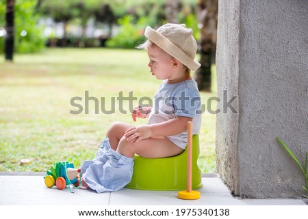 Sweet toddler boy, sitting on potty on a back porch in a holiday resort patio, playing with toys