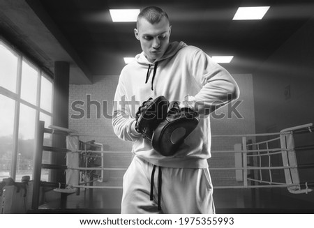 Male trainer in the gym against the background of the ring holds boxing paws. Mixed martial arts concept. High image quality