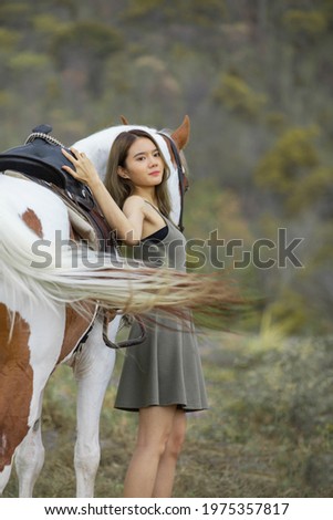 Asian women in a grey dress leaning happily side of horse on the field and mountains background