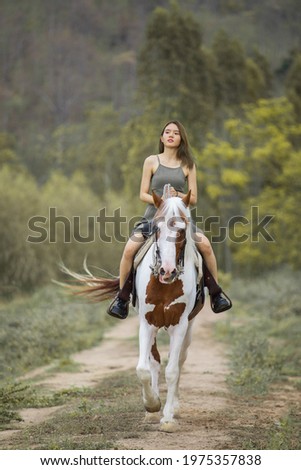 Asian woman in a grey dress is riding a brown white horse. On the Countryside Behind the mountains
