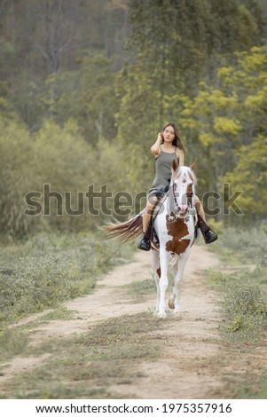 Asian woman in a grey dress is riding a brown white horse. On the Countryside Behind the mountains
