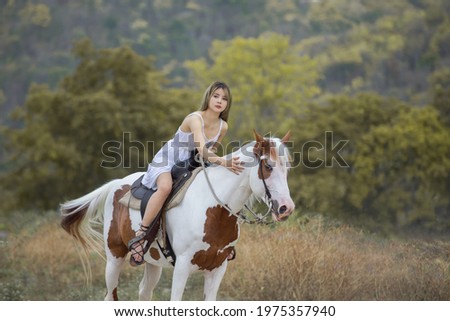 Asian woman in a white dress is riding a brown white horse. On the Countryside Behind the mountains