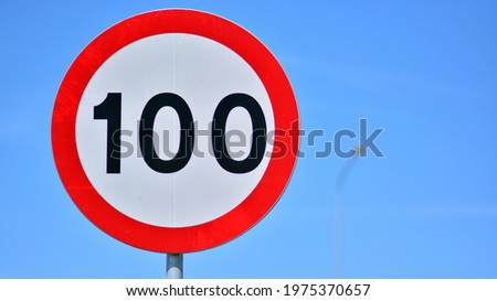 Road sign on a highway  indicates a speed limit of 100 km per hour. Red circle with white center.