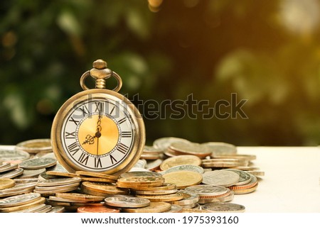 Retro vintage antique pocket watch clock on pile of coins. Money saving or time is money concept.
