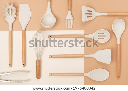 Pattern made from cooking utensil set. Silicone kitchen tools with wooden handle on beige background. Top view Flat lay. Royalty-Free Stock Photo #1975400042