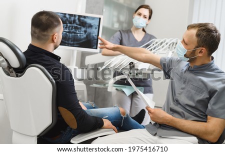 Male doctor and his male assistant shows the patient an x-ray image of his teeth at display. Computer diagnostics dental tomography. Planning teeth treatment in modern dental clinic