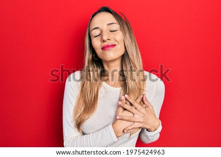 Beautiful hispanic woman wearing red diadem smiling with hands on chest with closed eyes and grateful gesture on face. health concept. 