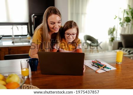 Beautiful smiling mom and cute daughter is using laptop and searching for cartoons.