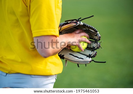 Close-up of a softball player's hand grasping a ball inside a baseball glove.
