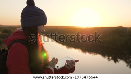 Carefree cheerful girl travels with a digital tablet in nature. Tourist blogger young woman with a navigator using a tablet computer on the top of mountain with a background of a beautiful landscape.