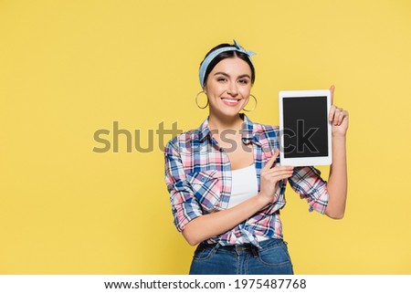 Smiling housewife holding digital tablet with blank screen isolated on yellow
