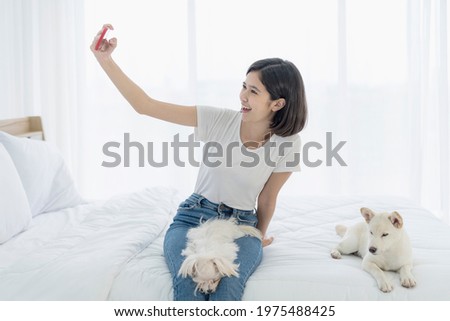 Young Asian women selfie with mobile phone. Young Asian women and girl were in bed with a dog. Girl and white Hokkaido inu dog and Maltese dog.