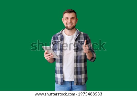 Young man with tablet computer showing thumb-up on color background