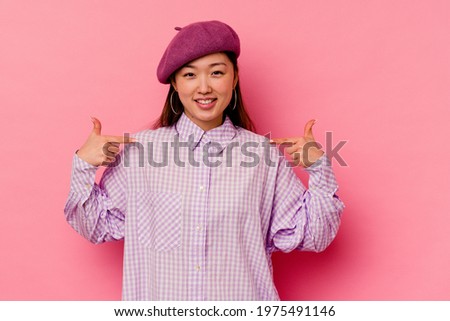 Young chinese woman isolated on pink background points down with fingers, positive feeling.