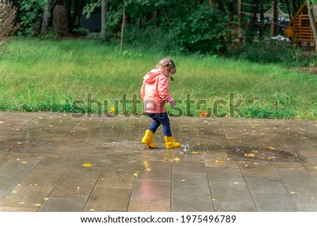 Little child girl walking in the rain in rainboots Royalty-Free Stock Photo #1975496789