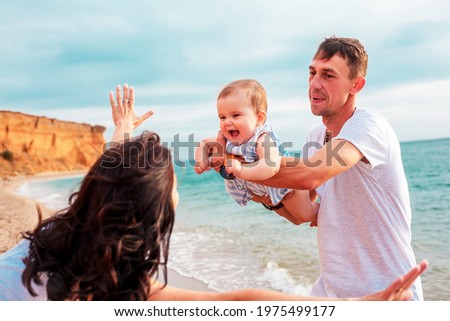 Happy active family together, mother, father and female toddler have fun in the shore of the beach, at the background sea or ocean. Parent holding a child 