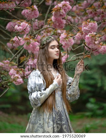 Young maiden in a medieval dress with sakura blossoms in a tropical garden