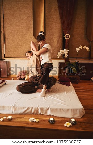 Smiling woman having her left arm stretched during Thai massage Royalty-Free Stock Photo #1975530737