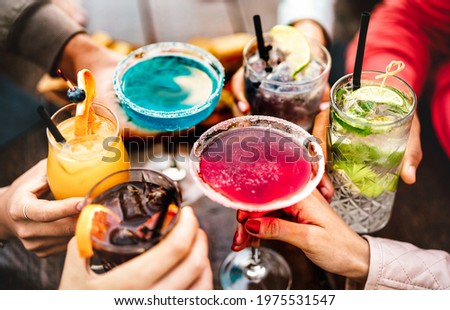 People hands toasting multicolored fancy drinks - Young friends having fun together drinking cocktails at happy hour - Social gathering party time concept on warm vivid filter - Shallow depth of field Royalty-Free Stock Photo #1975531547