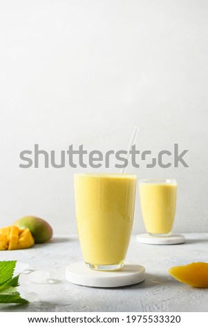 Indian ayurvedic mango lassie or lassi on light gray background. Vertical format. Mango lassie traditional healthy beverage with yogurt, water, spices, fruits and ice.