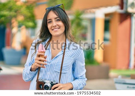 Young hispanic tourist woman using vintage camera and eating ice cream at the port.