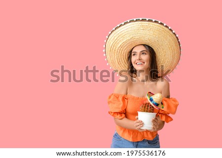 Beautiful young woman in sombrero hat and with cactus on color background Royalty-Free Stock Photo #1975536176