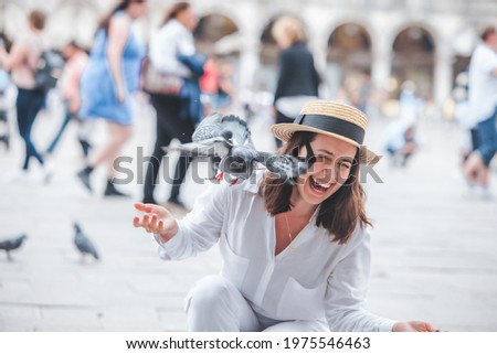 woman in white clothes with straw hat having fun with pigeons at venice city square piazza san marco