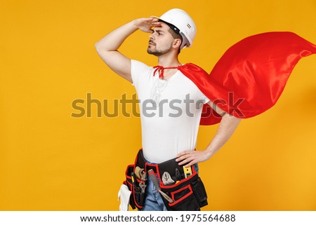 Powerful employee handyman man in superhero suit helmet hardhat hold hand at forehead look far away distance isolated on yellow background studio Real heroes defend you. Repair home renovation concept