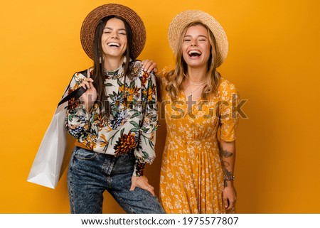two beautiful attractive stylish women friends having fun together wearing straw hat summer fashion style trend dress and printed shirt posing on yellow background isolated