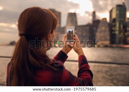 Woman taking a photo with a cell phone to the syline in Manhattan