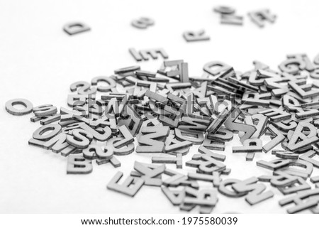 Little wooden letters of latin alphabet cut from thin plywood with a laser cutter piled randomly in a pile on a white background. BW photo.