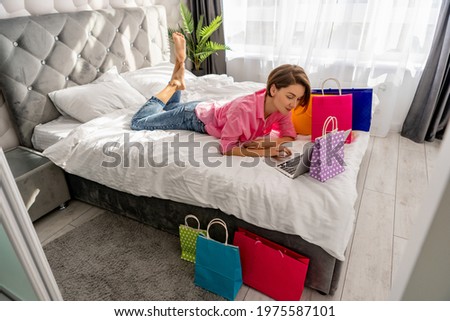 pretty happy woman lying on bed at home with colorful shopping bags on black friday sale discount excited buying online using laptop