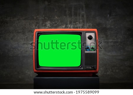 Retro old TV with green screen on wooden box in front of old wall background.