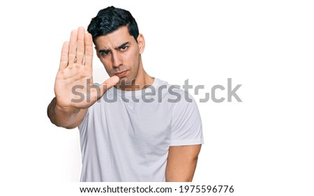 Handsome hispanic man wearing casual white t shirt doing stop sing with palm of the hand. warning expression with negative and serious gesture on the face. 