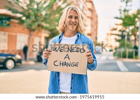 Young scandinavian activist man smiling happy holding we need a change banner at the city.