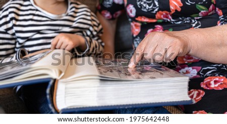 A grandmother with her little granddaughters looks at family photos in photo albums.