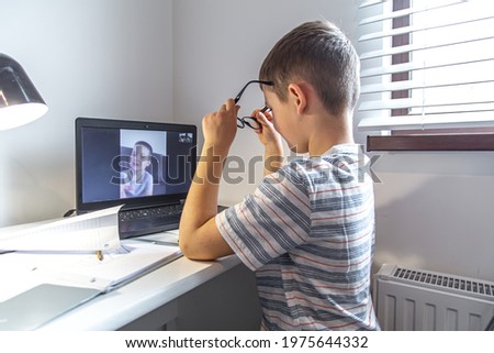An elementary school student sits at a desk in front of a laptop and communicates via video link online at home.