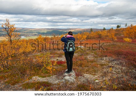 A woman from backside standing on a mountain and taking pictures of beautiful autumn nature of Norway