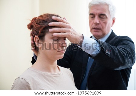 Mature gray-haired man hypnotizes Caucasian woman during hypnotherapy session. The psychologist uses alternative treatments for the subconscious mind Royalty-Free Stock Photo #1975691099