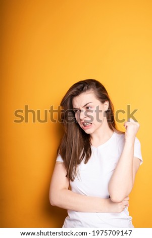 Annoyed young girl in a white t-shirt with braces suffers from pain in the teeth while standing on a yellow background