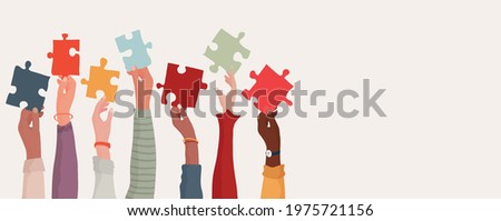 Group of multi-ethnic business people with raised arms holding a piece of jigsaw. Colleagues of diverse races and culture. Cooperate and collaborate. Concept of teamwork and success Royalty-Free Stock Photo #1975721156