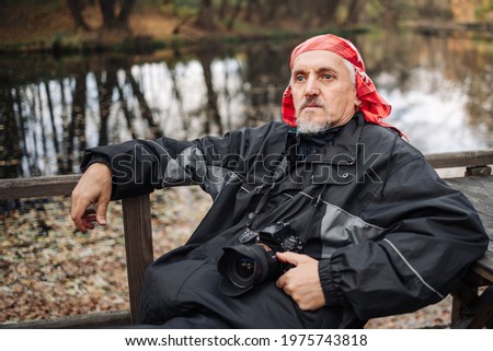 Mature male photographer resting after shooting in a city park with a pond