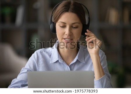 Remote consultant. Confident millennial female client support assistant sit at workplace by laptop wear headset consult caller. Young female call center operator work online answer customer question Royalty-Free Stock Photo #1975778393