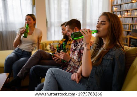 A group of young friends hanging out together on a house party while drinking beer while using smartphones